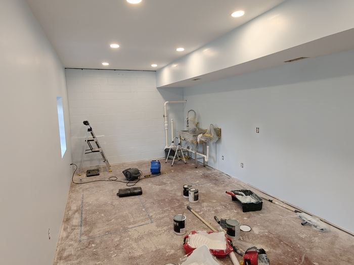 Interior room renovation with painted walls, recessed lights, ladders, and painting supplies.